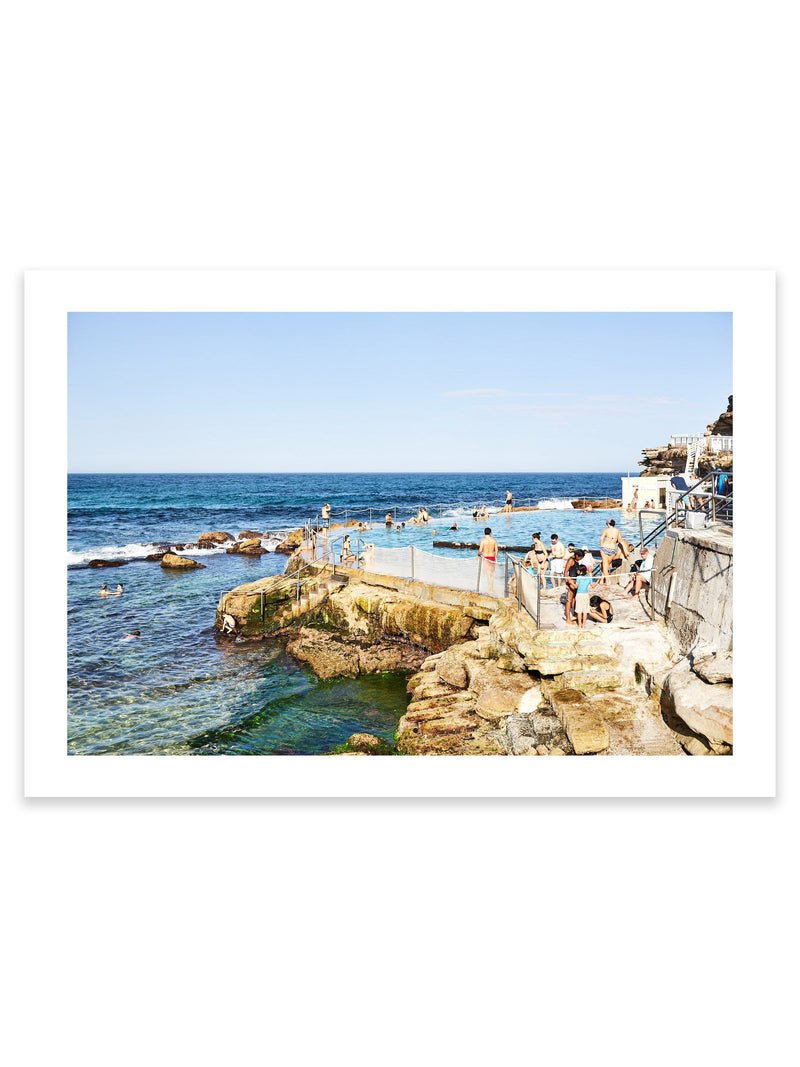 This coastal, summer, tropical, beach landscape print artwork features rolling ocean waves and a blue sky overlooking the Bronte rockpool swimming pool, located close to Bondi Beach and Icebergs beach club in Sydney, Australia. This print option a white border (measuring between 5cm and 4cm depending on print size selected) so the print will have a white border framing the print when it is framed.