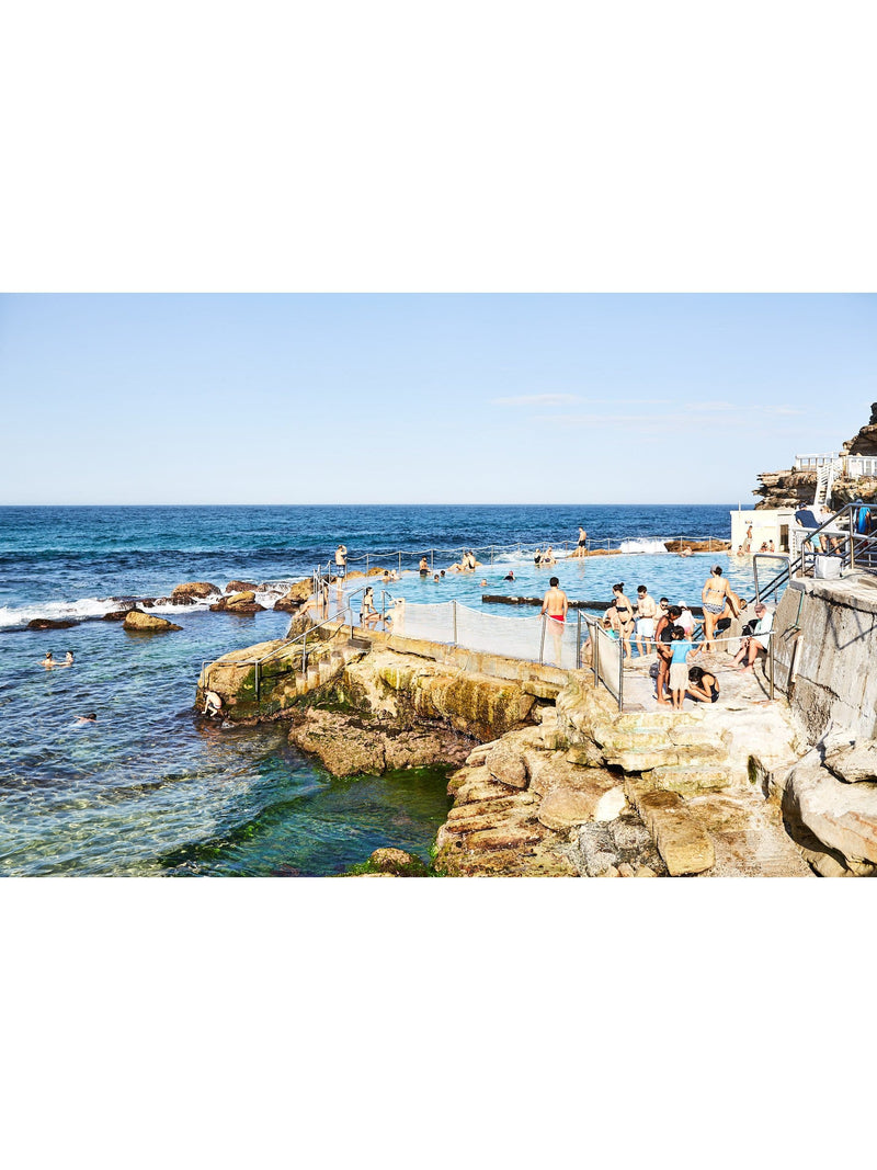 This coastal, summer, tropical, beach landscape print artwork features rolling ocean waves and a blue sky overlooking the Bronte rockpool swimming pool, located close to Bondi Beach and Icebergs beach club in Sydney, Australia. This print option has no border (is full bleed) so the print goes all the way to the edge when framed.